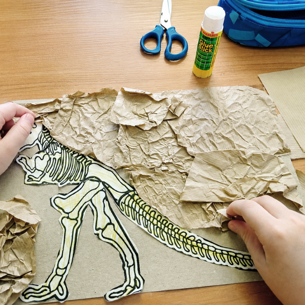 Przedszkolak podczas przygotowania wyklejanki z papieru i kartonu na Dzień Dinozaura używający kleju w sztyfcie AMOS