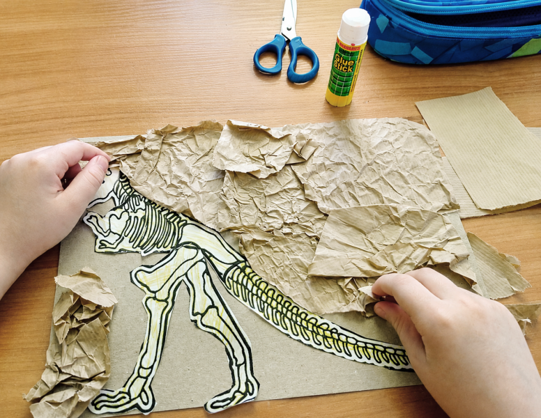 Przedszkolak podczas przygotowania wyklejanki z papieru i kartonu na Dzień Dinozaura używający kleju w sztyfcie AMOS